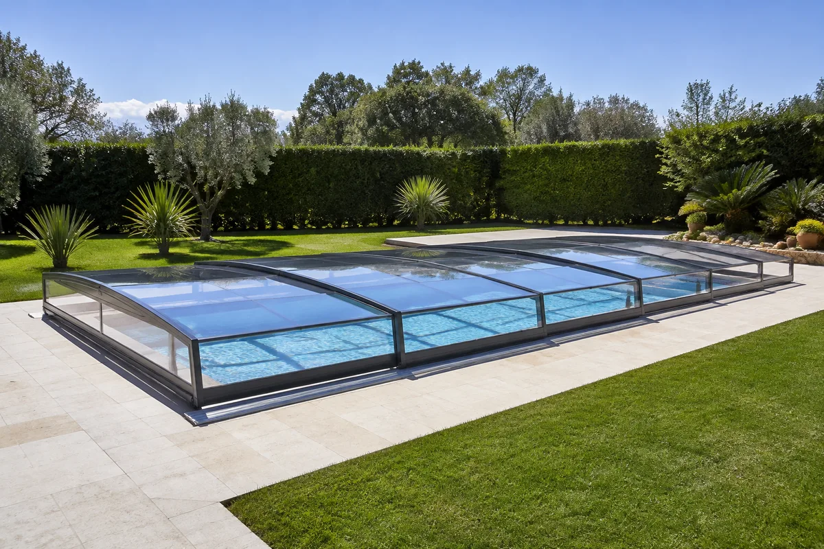 Abri de piscine bas en polycarbonate transparent fermé sur un bassin, jardin ensoleillé