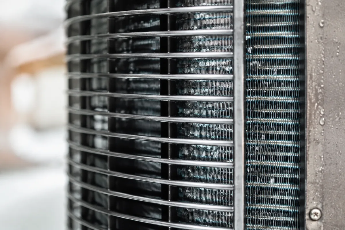 Échangeur et ventilateur d&rsquo;une pompe à chaleur de piscine vus de près, grille métallique visible